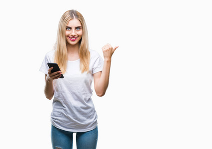 年轻漂亮的金发女人用智能手机在孤立的背景上指指点点，并用拇指向侧面展示，脸上洋溢着幸福的笑容