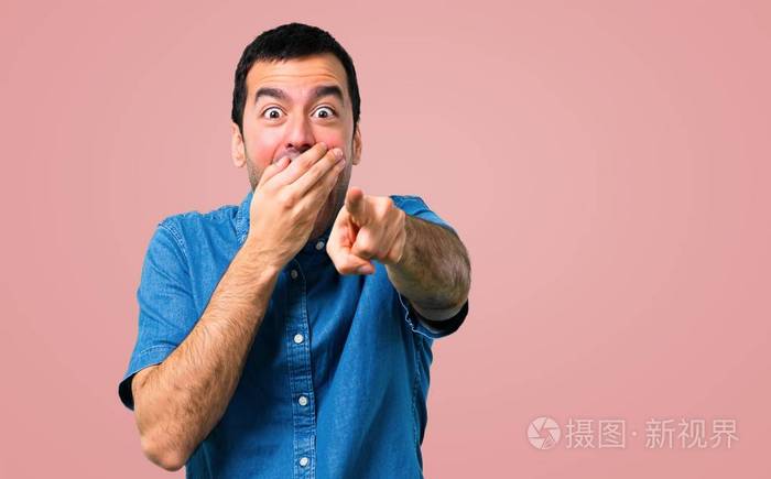 一位穿着蓝色衬衫的帅哥用手指指着某人在粉红色的背景下笑了很多