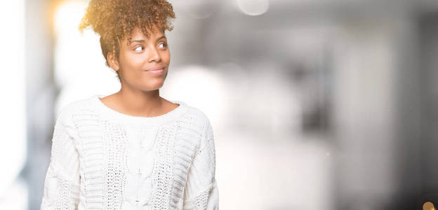 美丽的年轻非洲裔美国妇女穿着冬天的毛衣，在孤立的背景上微笑着看着一边，凝视着远方的思考。