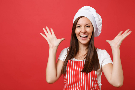 家庭主妇女厨师或面包师穿红色条纹围裙，白色T恤，厨师帽子隔离在红墙背景上。 特写管家黑发女人的肖像。 模拟复制空间概念