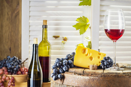 仍然生活的红酒与木制桶。 一瓶红酒，在一个旧的木桶上放着奶酪和葡萄。 品酒和生产理念。