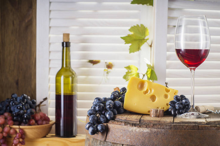 仍然生活的红酒与木制桶。 一瓶红酒，在一个旧的木桶上放着奶酪和葡萄。 品酒和生产理念。