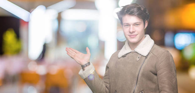 年轻的英俊男子穿着冬衣，在孤立的背景上微笑，欢快的呈现，用手掌指着相机。