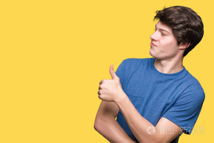 年轻的帅哥,穿着蓝色t恤,在孤立的背景上看着骄傲的微笑,竖起大拇指