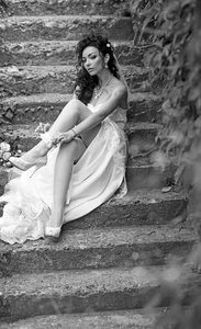 新娘化妆和发型的女孩。女人在腿上戴花边袜。的女人在丝袜内衣在婚礼当天。穿着白色连衣裙的新娘坐在户外台阶上。婚纱时尚及配件