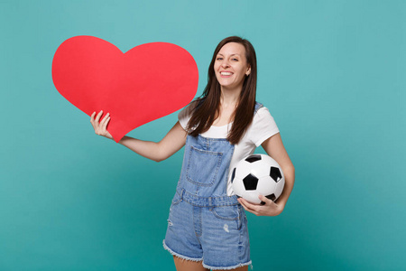 微笑的年轻女子足球迷振作起来，支持最喜欢的球队与足球空空白的红色心脏隔离在蓝色绿松石背景上。 家庭休闲生活方式观念