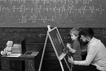 学生与老师在学校。侧面看父子学算术。爸爸向可爱的孩子解释方程式