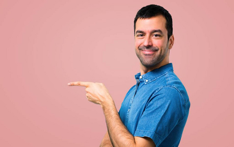 一个英俊的男人，穿着蓝色衬衫，手指指向一边，在粉红色的背景上展示一种产品