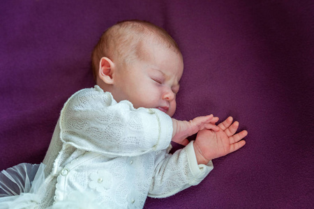 柔和的肖像和平甜蜜的新生婴儿躺在床上，睡在紫色的毯子背景。 甜蜜的梦晚安。 儿童保育概念