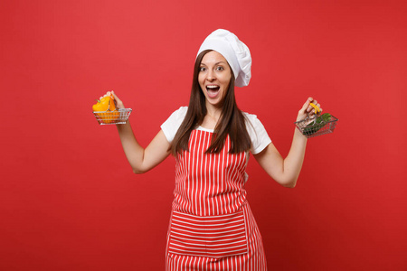 家庭主妇女厨师厨师面包师穿条纹围裙，白色T恤，厨师帽子隔离在红墙背景上。 女人拿着黄椒黄瓜在购物车模拟复制空间概念