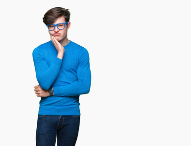 年轻的英俊男子戴着蓝色的眼镜，在孤立的背景下思考，看起来疲惫，厌倦了交叉双臂的抑郁问题。