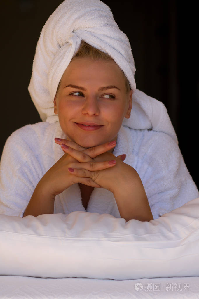 迷人的金发女孩穿着白色浴袍在旅游胜地洗澡后放松