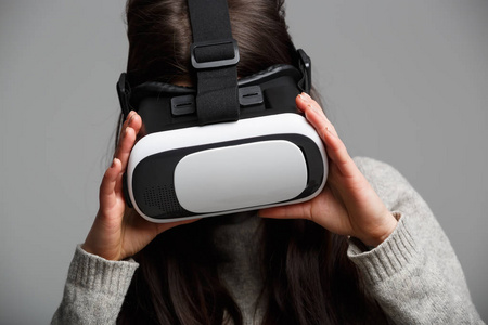 年轻的黑发女孩在玩虚拟现实护目镜用于移动游戏应用。女孩使用带有创新3D VR耳机的移动游戏应用程序。趋势增强现实小工具正在使用中