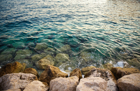 清澈的海水在日落时冲刷着岩石海滩。阳光明媚的克罗地亚里维埃拉的美丽自然。暑假旅行的目的地背景。亚得里亚海海岸壁纸