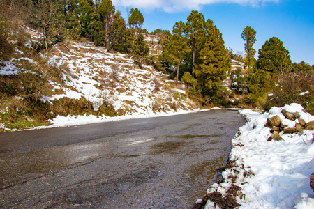 上坡路在巴尼基特达尔豪西希马恰尔邦，印度，侧面充满了雪。 风景优美的冬季景观，从沥青路上覆盖着白雪和树木，在蓝天背景和云彩的道路