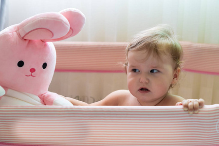 可爱的笑婴儿站在粉红色的床上。为小孩子准备的粉红托儿所。一个小女孩学会了站在她的婴儿床里。一个婴儿站在阳光明媚的卧室的婴儿床里。