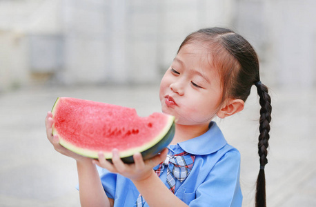 可爱的亚洲小女孩穿着校服喜欢吃西瓜。