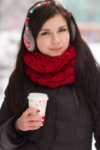 在明亮的冬日里，年轻的黑发女人在户外捧着咖啡杯