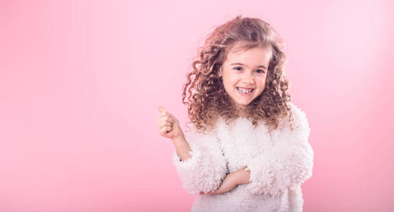 一个可爱的微笑小女孩的肖像，卷发指向粉红色的背景