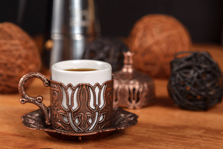 装饰丰富的小传统土耳其浮雕铜杯，用于木制背景上的浓黑咖啡与金属咖啡壶。 咖啡馆的咖啡概念。