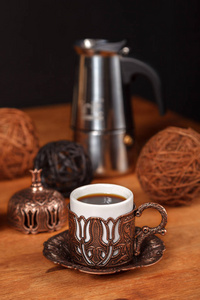 装饰丰富的小传统土耳其浮雕铜杯，用于木制背景上的浓黑咖啡与金属咖啡壶。 咖啡馆的咖啡概念。