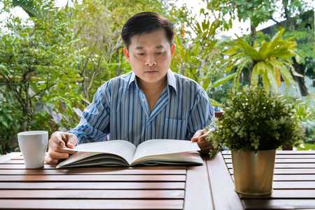 一个中年亚洲男人在后院看书照片
