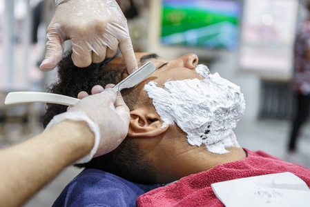 理发店用剃须刀刮胡子的理发师用理发店用刮胡膏覆盖着年轻的黑人脸上