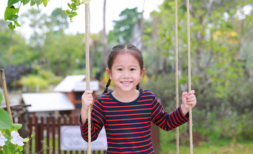 特写快乐的亚洲小女孩玩耍，坐在自然公园的秋千上。