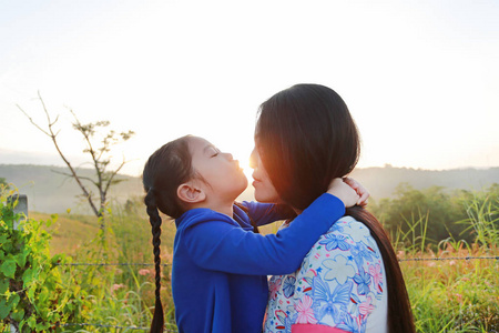 在早晨日出时，关闭亚洲母亲和女儿在草地上接吻。