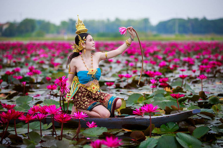 红莲花田池塘木船上穿着金娜蕾服装的美丽女子，想象形象遵循泰国传统和泰国童话