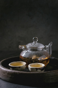 热绿茶在两个传统的中国粘土陶瓷杯和玻璃茶壶站在托盘上的黑色大理石桌子。