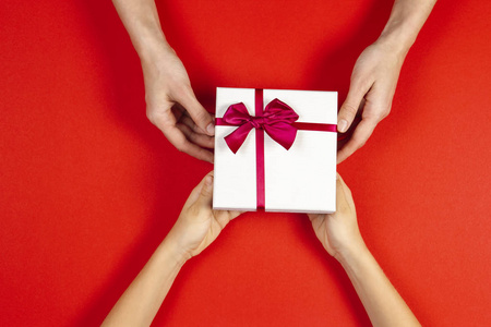 两个人的手给和接收礼物礼物盒的顶部看法与丝带在红色背景.