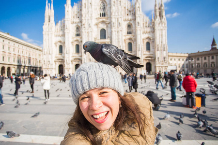 冬季旅行假期和鸟类概念年轻快乐的女游客与有趣的鸽子在米兰著名的杜莫大教堂前自拍照片。