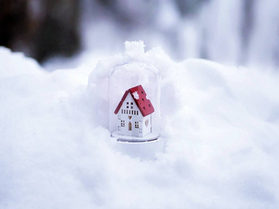 一个小玩具装饰白色的房子，有一个红色的屋顶，雪上有灯光照明，冬季季节性假日的概念，圣诞节，新年的新房子，家庭舒适