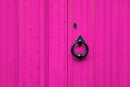 粉红色门上的黑色伪造手柄。 带铁柄的旧古董门。