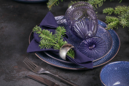 圣诞餐桌设置。 深蓝色装饰与杉树枝。 盘子酒杯和餐具与装饰纺织品在黑暗的背景。