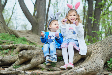 可爱有趣的女孩和男孩带着复活节彩蛋在公园。 复活节的概念。 孩子们在复活节玩复活节彩蛋。 家庭假日