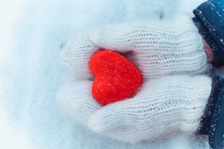女性手在编织白色手套与雪的心脏在冬天天