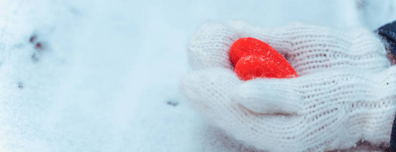 女性手在编织白色手套与雪的心脏在冬天天