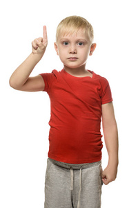 穿着红色T恤的金发男孩站着，食指向上指向。 在白色背景下分离