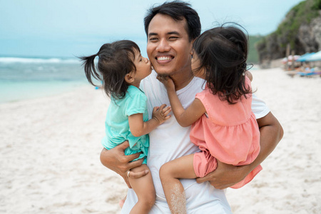 两个小女孩一起在海滩上和他父亲接吻