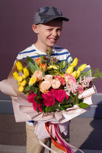 微笑的小男孩站着一束花。 给妈妈的美丽的花。