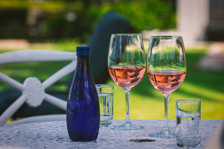 花园里的桌子上有两杯玫瑰酒和一瓶蓝色的水