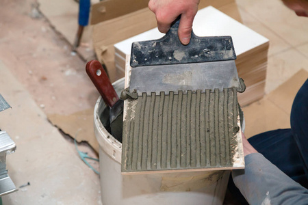 s hand smears cement glue on the ceramic tile with trowel to glu