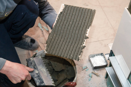 s hand smears cement glue on the ceramic tile with trowel to glu