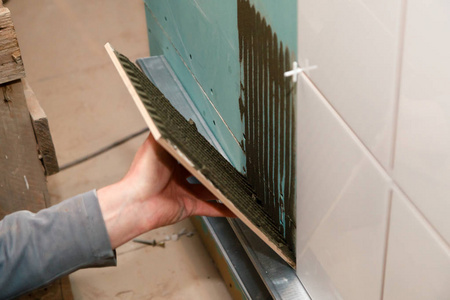 s hand glues ceramic tile with adhesive in the bathroom. Concept