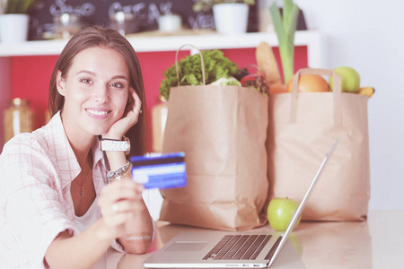 微笑的妇女在线购物使用平板电脑和信用卡在厨房。微笑的妇女