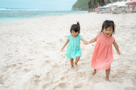 两个小女孩在海边走在白沙上时牵手