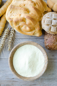 不同种类的传统意大利新鲜烘焙面包和面包与碗面粉在木桌背景。 乡村复古风格。 上面的风景。