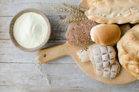 不同种类的传统意大利新鲜烘焙面包和面包与碗面粉在木桌背景。 乡村复古风格。 上面的风景。